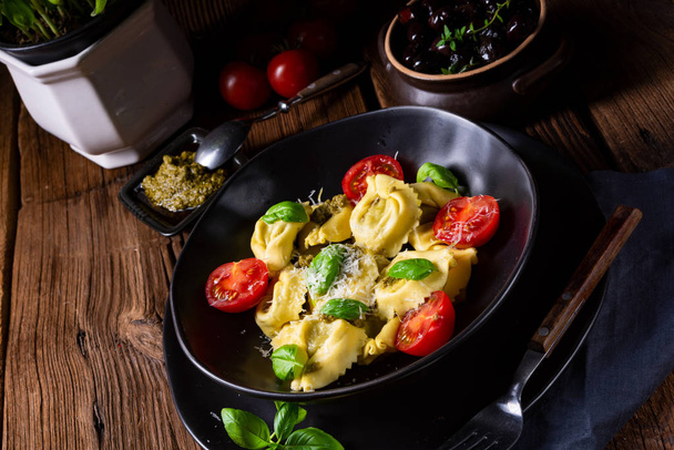 rustic spinach tortellini with cheese and tomatoes on black plate  - Φωτογραφία, εικόνα