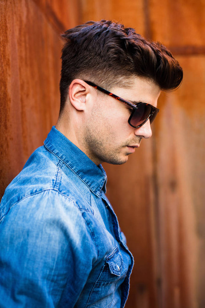 close up portrait of a sexy man with suglasses and jeans shirt on a rusty background, looking confident - Foto, Imagen