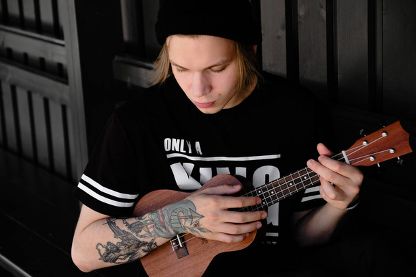 Young man playing on acoustic guitar or ukulele outdoor - Foto, Imagen