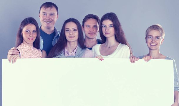 Happy young group of people standing together and holding a blank  - Photo, Image