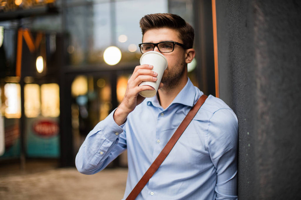 caffee break. handsome smart casual man with eyeglasses and leather bag having a take away coffee in urban area outside - Фото, изображение