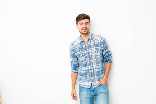 Netter Kerl, junger Mann, der in Jeans und kariertem Hemd an einer weißen Wand steht, mit Leerraum - Foto, Bild