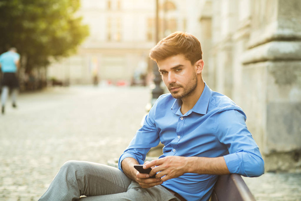 elegant man in blue shirt, using his cellphone outside o a bench - Φωτογραφία, εικόνα