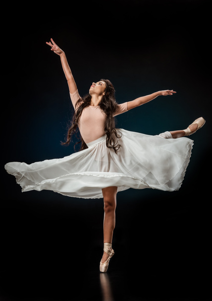 elegant female ballet dancer in white skirt dancing on dark background - Фото, зображення