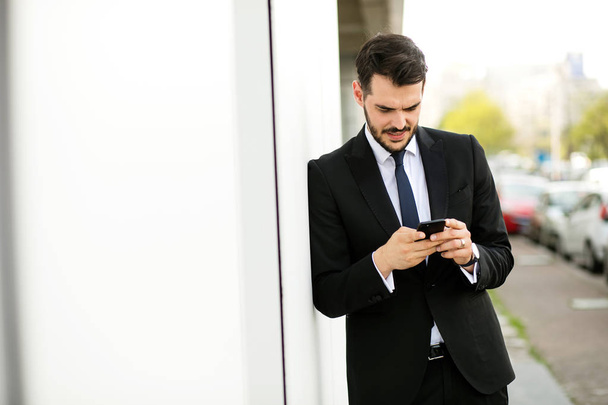 handsome elegant man in suit using his cellphone and smiling, reciving good news - Zdjęcie, obraz