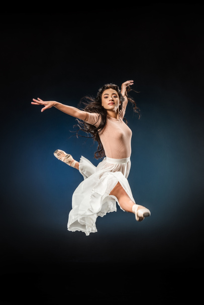young ballerina in elegant clothing jumping on dark backdrop - Foto, afbeelding