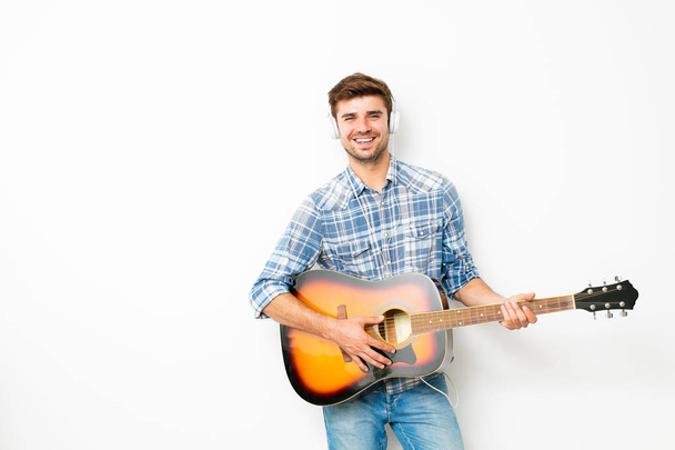 hobby for boys. man playing the guitar with headsets on his head, enjoying his spare time in his own house, doing what he likes, on white background - Foto, Bild