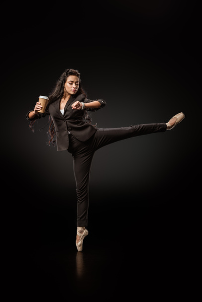 atractiva joven empresaria en ropa formal y zapatos de ballet con café para ir a comprobar la hora en el fondo negro
  - Foto, Imagen