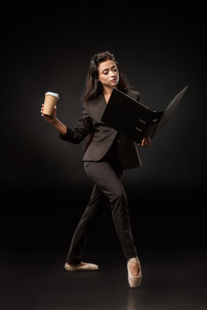 attractive businesswoman in suit and ballet shoes with folder and coffee to go posing on black backdrop - Photo, Image