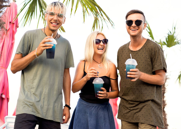 three friends cheerful company rest on a tropical beach and drink cocktails, very, magazine concept - Photo, image