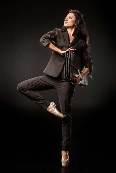 красивая женщина в костюме и балетной обуви с чемоданом позирует на черном фоне
 - Фото, изображение