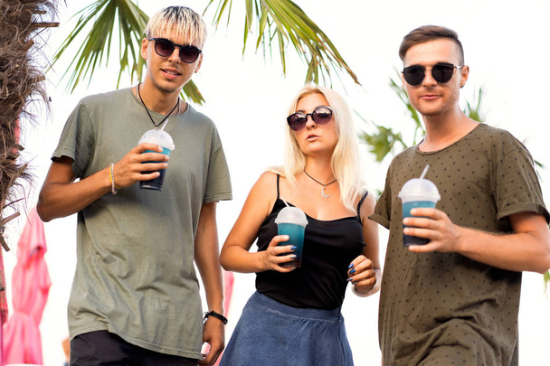 three friends cheerful company rest on a tropical beach and drink cocktails; very; magazine concept - Photo, image