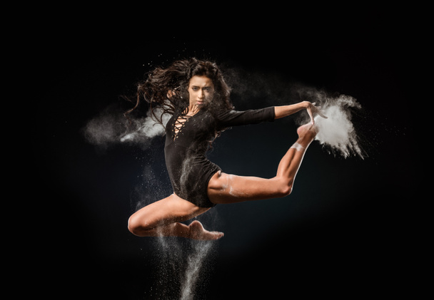 bela bailarina em bodysuit preto com talco em pó pulando no fundo escuro
 - Foto, Imagem