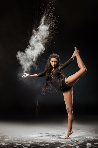 joven bailarina en body negro con talco en polvo bailando sobre fondo oscuro
 - Foto, Imagen