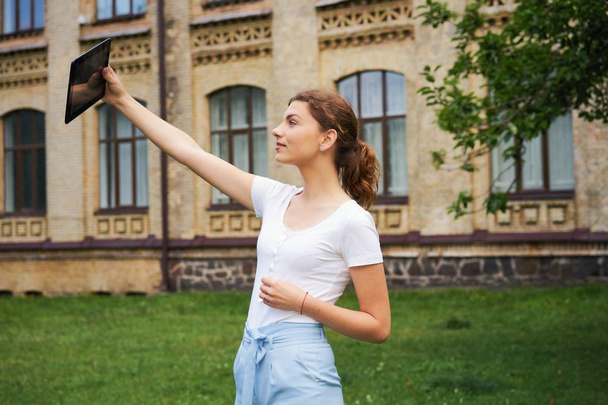  young Caucasian  beautiful woman with tablet pc taking selfie in park           - Zdjęcie, obraz