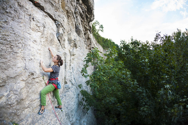 Nainen treenaa luonnossa. Aktiivinen elämäntapa. Tyttö kiipeää kalliolle. Kiipeilijä voittaa vaikean kiipeilyreitin
. - Valokuva, kuva