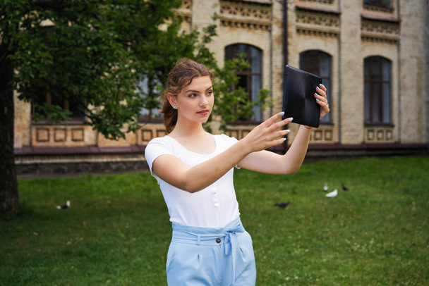 young Caucasian  beautiful woman with tablet pc taking selfie in park           - Foto, Imagem