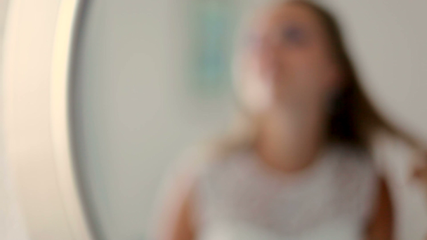 Joven rubia atractiva con vestido blanco se pone pendientes delante del espejo
 - Imágenes, Vídeo