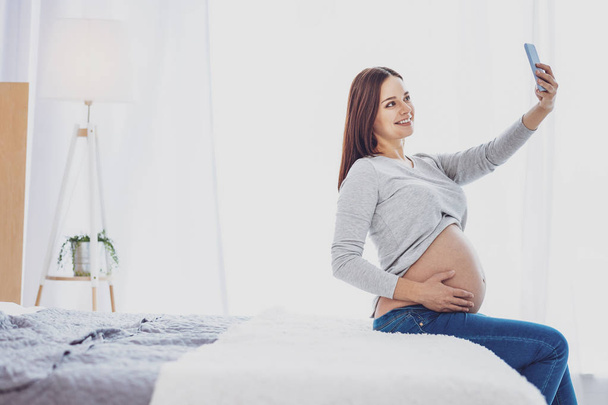 Delighted pregnant woman making selfie in bed room - Foto, Imagem