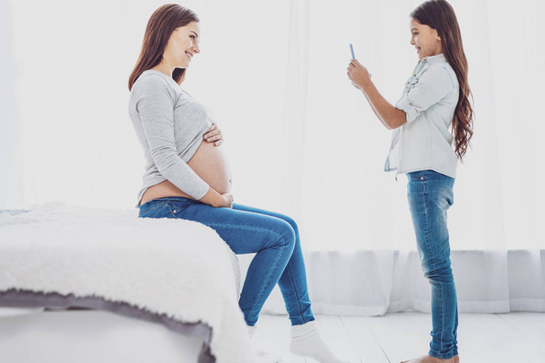 Cute little daughter photographing her adorable pregnant mother - Photo, Image