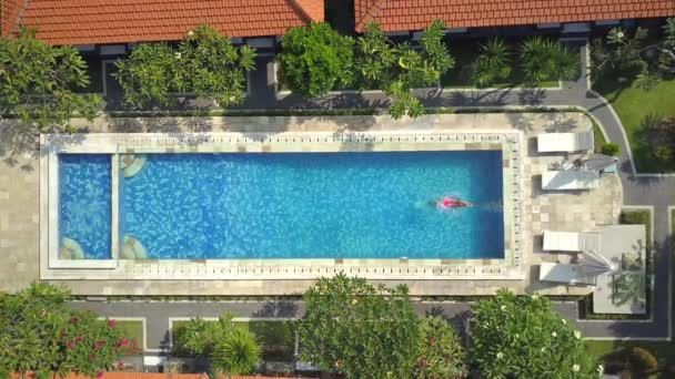 Antenne von oben nach unten: Unerkennbare Frau im Sommerurlaub springt zur Erfrischung an einem heißen, sonnigen Tag kopfüber ins Pool-Wasser. Mädchen im rosa Bikini taucht und schwimmt in leerem Pool im Luxus-Resort - Filmmaterial, Video