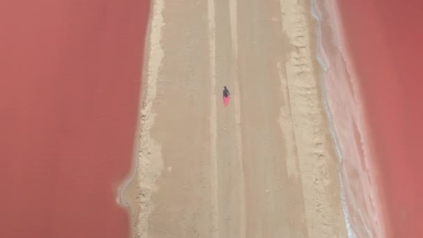 CERRAR AERIAL: Mujer irreconocible caminando a lo largo del dique arenoso rodeado por el agua naranja preciosa de las salinas de Las Colorado en el día soleado caliente en México. Chica turística paseando por los estanques de sal
 - Metraje, vídeo