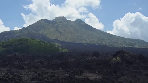 Luchtfoto Zoom-In Effect ruwe steenachtige zwarte lava terrein en grijze gewone vulkanische bodem bij de toeten van Gunung Batur naar het hoogtepunt van de bergketen. Dramatische landschap op Kintamani vulkaan krater, Bali - Video