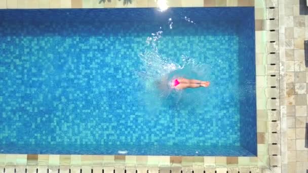 AERIAL CERRAR ARRIBA ARRIBA: Mujer joven en vacaciones de verano saltando de cabeza en el agua clara de la piscina azul para refrescarse en el día soleado caliente. Chica en bikini rosa buceando en una piscina vacía en un resort de lujo
 - Metraje, vídeo