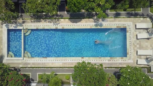 AERIAL SLOW MOTION TOP DOWN: Mulher em férias de verão saltando cabeça primeiro na água da piscina azul para refresco no dia ensolarado quente. Menina de biquíni rosa mergulho e natação na piscina vazia no resort de luxo
 - Filmagem, Vídeo