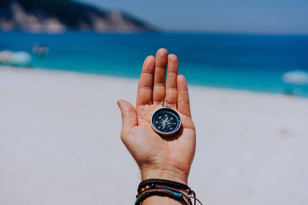 One open stretched hand palm with black metal compass on the sandy beach. Find your wish goal way concept. Blue sea in background. Point of view pov - Fotó, kép
