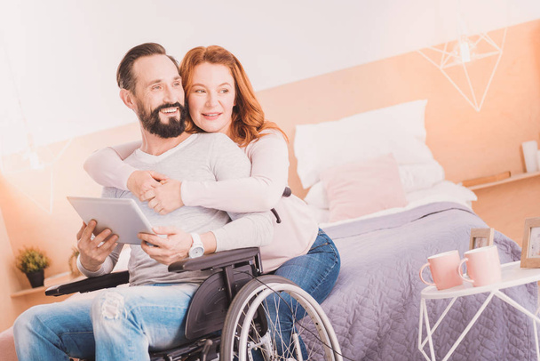 Iloinen pyörätuolilla mies käyttää tabletin vaimonsa kanssa
 - Valokuva, kuva