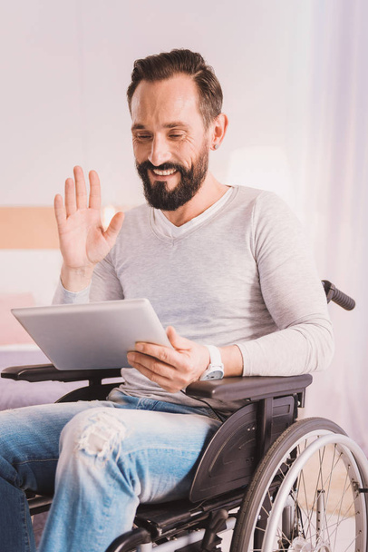 Cheerful wheelchaired man uisng a tablet for communication - Foto, Bild