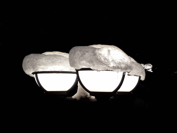 V temnotě noci jasné světlo lucerny podporuje a svítí na cestu. Tři stráže střežící proti temnotě, oblečený ve třech sněhová čepice. - Fotografie, Obrázek