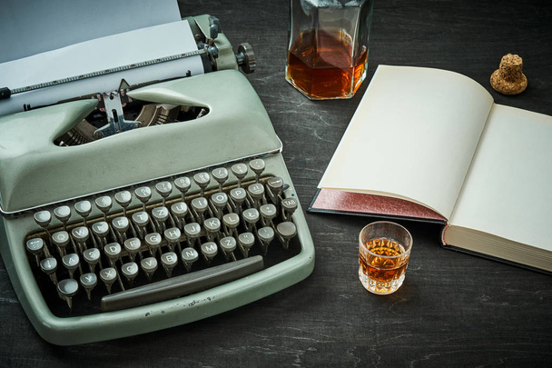 bela velha máquina de escrever cinza, livro e um copo com álcool
 - Foto, Imagem