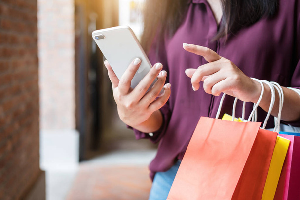 Consumerism, shopping, lifestyle concept, Young woman holding colorful shopping bags and smartphone enjoying in shopping. - Foto, imagen