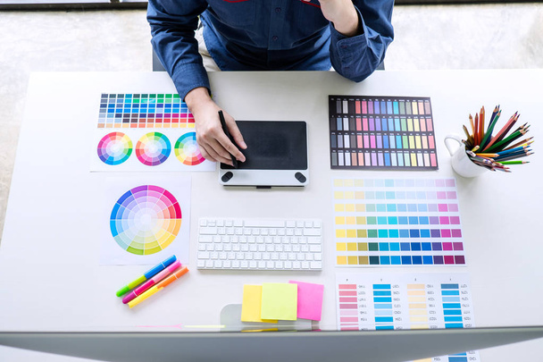 Image of male creative graphic designer working on color selection and drawing on graphics tablet at workplace with work tools and accessories, top view workspace. - Photo, Image