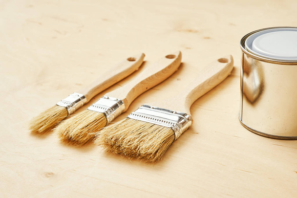 three brushes and a silver paint can on a wooden board - Foto, Imagem