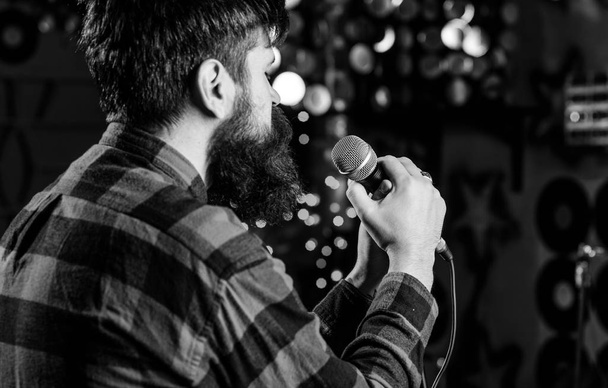 Musician with beard singing song in karaoke, rear view. Man in checkered shirt holds microphone, singing song, karaoke club background. Guy likes to sing in dark karaoke hall. Rock singer concept - Photo, image