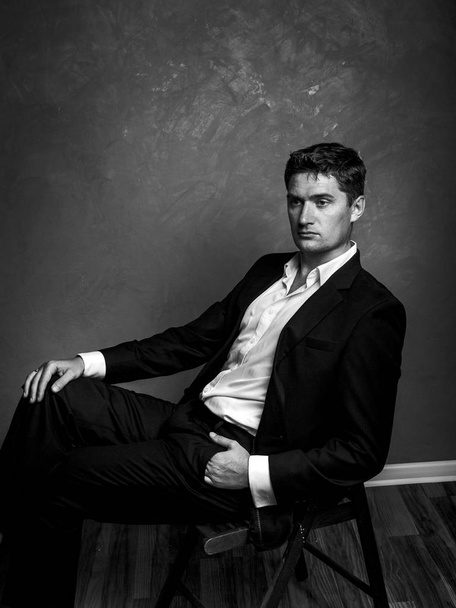 Handsome man in a business suit sits on a chair and looks away, style fashion black and white portrait - Photo, image