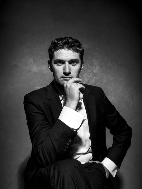 Elegant gentleman in a business suit sits on a chair, a creative stylish male portrait, a frontal view - Fotó, kép
