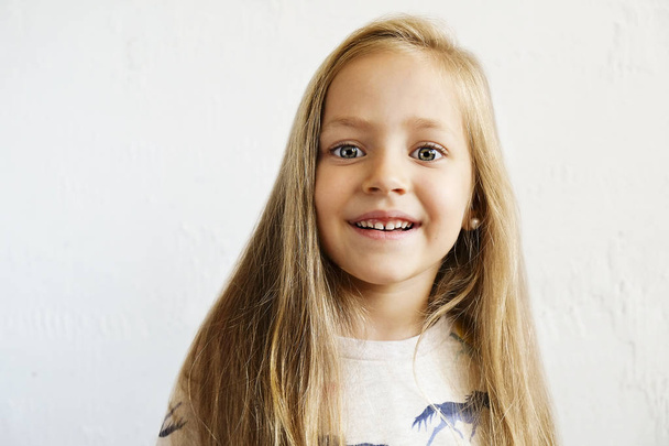 Portrait of happy little girl with long blonde hair smilng and showing positive emotions. Funny child with joyful facial expression. White isolated background, close up, copy space. - Φωτογραφία, εικόνα