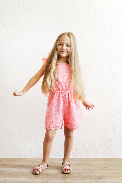 Little blonde girl with long golden hair dancing, smling and having fun over white textured plaster wall background. Five years old blonde female child posing. Copy space for text. - Photo, image