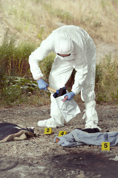 Criminologist technician in DNA free protective suit collecting evidences of probable criminal act - Photo, image