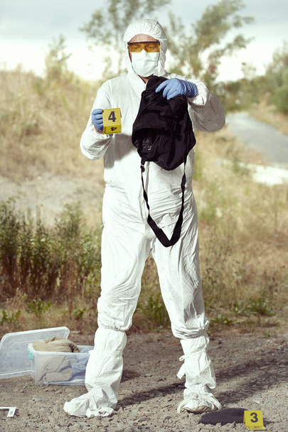 Criminologist technician in DNA free protective suit collecting evidences of probable criminal act - Foto, imagen
