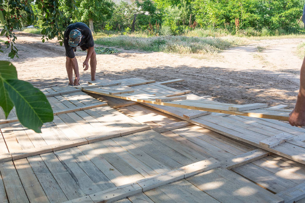 Чоловік будує дерев'яний паркан. Робітники підбирають дерев'яні дошки для опалубки паркану. Дерев'яні опалубки для бетону на будівельному майданчику
. - Фото, зображення