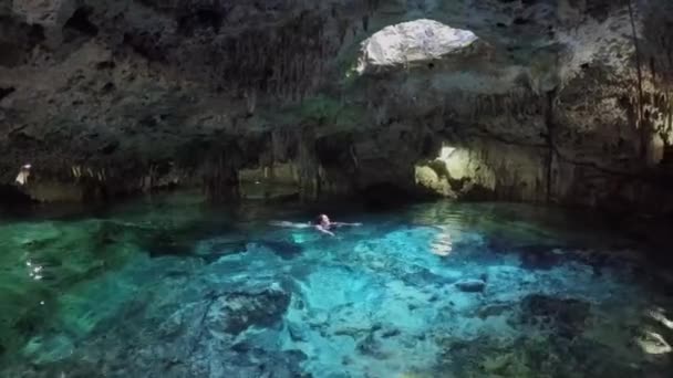 Jeune femme nageant dans une piscine turquoise dans une grotte souterraine magique avec la lumière du soleil provenant du trou dans le plafond. Architecture fascinante des stalactites et stalagmites à Aktun Chen cenote
 - Séquence, vidéo