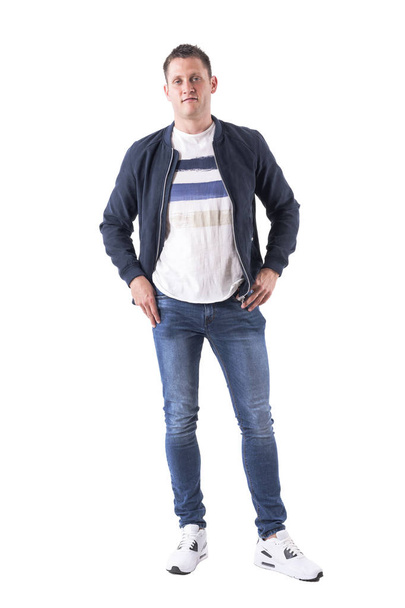 Cool young adult relaxed guy in bomber jacket posing with hands in pockets looking at camera. Full body isolated on white background. - Fotografie, Obrázek