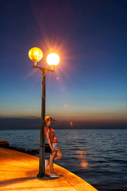 Sání Asijské twink žena pózuje s pouliční lampa na nábřeží v Poreč, Chorvatsko. Noční scéna. Cíl cesty. - Fotografie, Obrázek