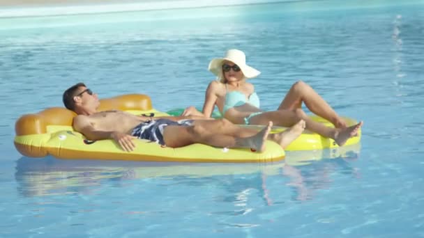 FERMER : Convient aux jeunes couples posant et se relaxant sur des floaties de pizza et d'ananas dans la piscine. Petite amie et petit ami profitant de vacances d'été sur des flotteurs colorés amusants flottant dans l'eau par une chaude journée ensoleillée
 - Séquence, vidéo