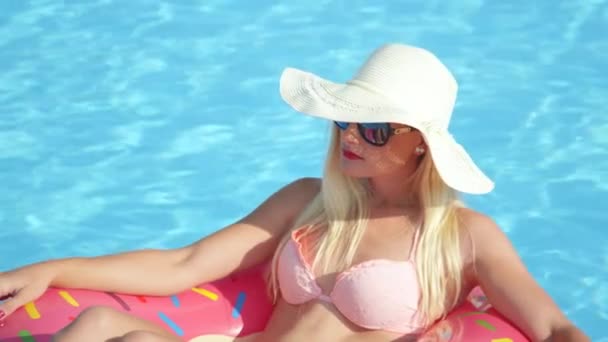 SLOW MOTION SULJE: Kaunis blondi tyttö rentouttava puhallettava vaaleanpunainen donitsi float. Nuori nainen kauneus bikinit nauttia kesäloma vaaleanpunainen kellua uima-altaassa kuuma aurinkoinen päivä
 - Materiaali, video
